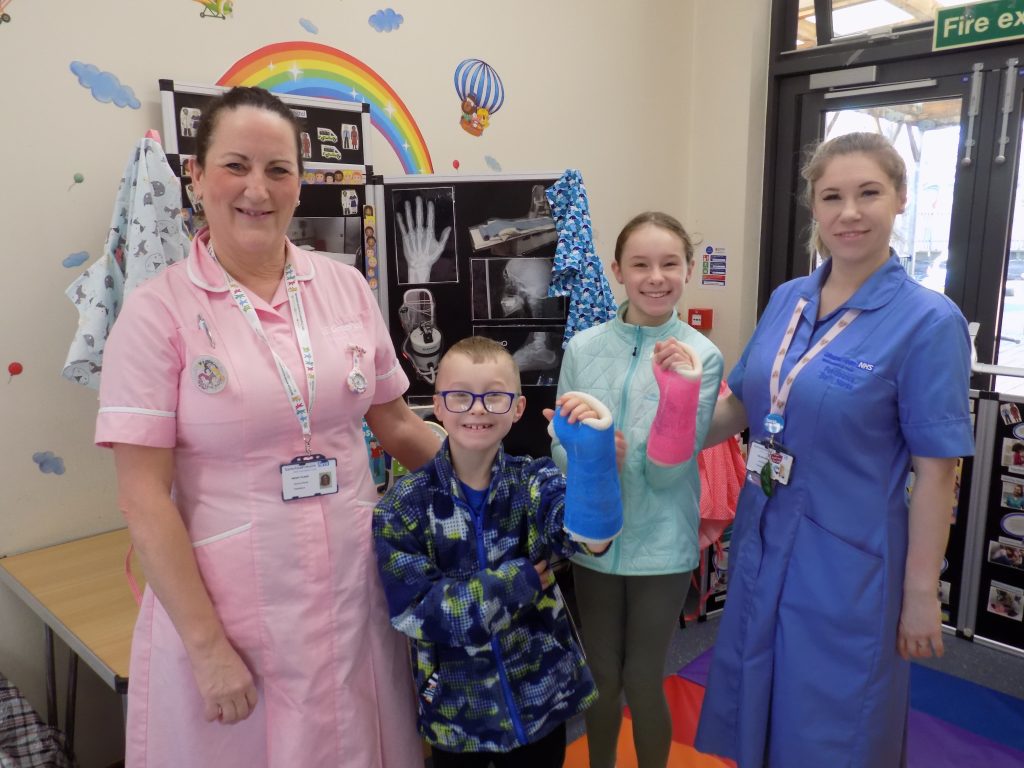 A picture of two of the children's nursing team with a young boy and girl who are wearing plaster casts.