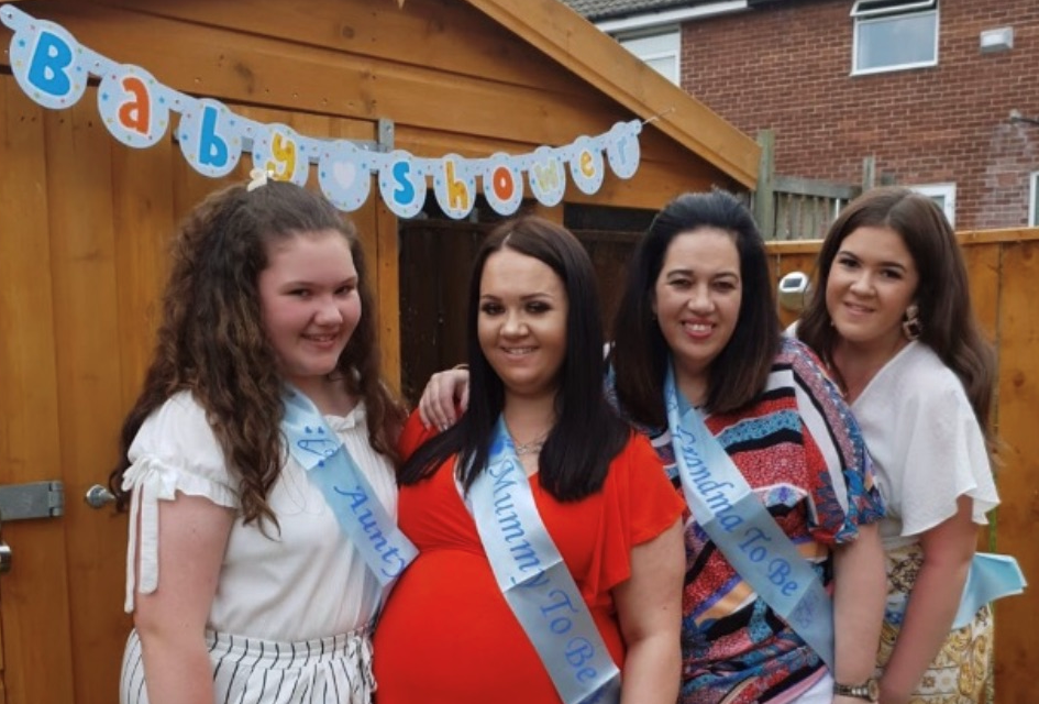 Tricia Hughes with her family in a garden in front of bunting that reads baby shower