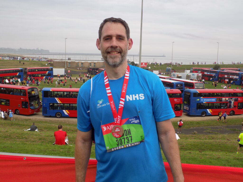 male runner with beard in front of buses with medal