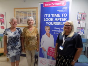 Brenda and Ann with the Breast Cancer Team stood next to a breast screening poster