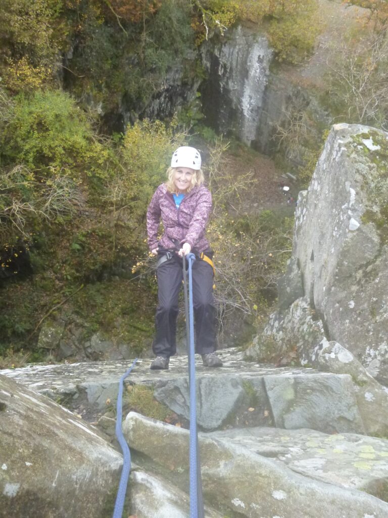 photo of woman in a pink coat abseiling down a cliff