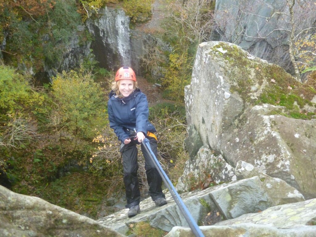 photo of woman in climbing gear abseiling down a cliff