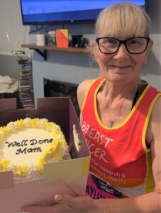 Photo of Hayley, one of our Charity runners. She is wearing a running vest and holding a cake with the words "well done mam" iced on the top.