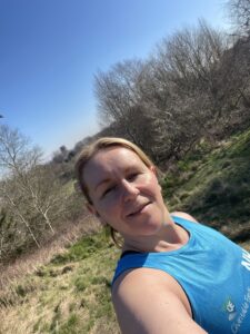 Selfie photo of Karen, one of our Charity runners. The photo is taken on a sunny day with trees and grassland in the background.