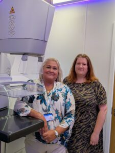 Two health works stand next to a mammogram machine