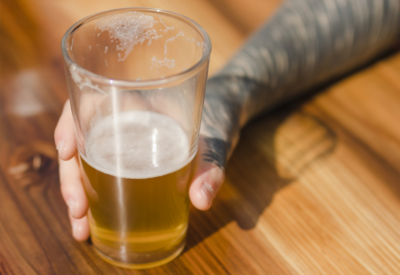 A pint glass of beer, half full on a bar.