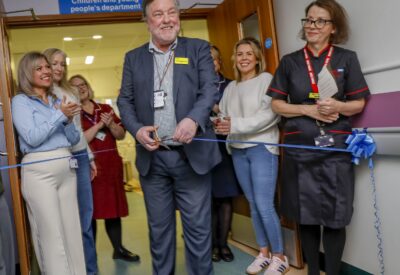 Photo of a group f staff and patients at the official opening with Sir Paul Ennals cutting the ribbon