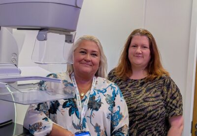 Two health works stand next to a mammogram machine