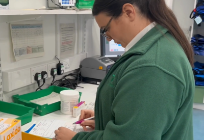 A pharmacist in a green coat checking a prescription for a patient