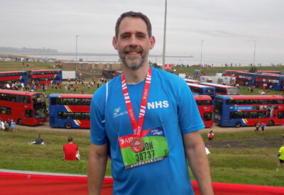 male runner with beard in front of buses with medal